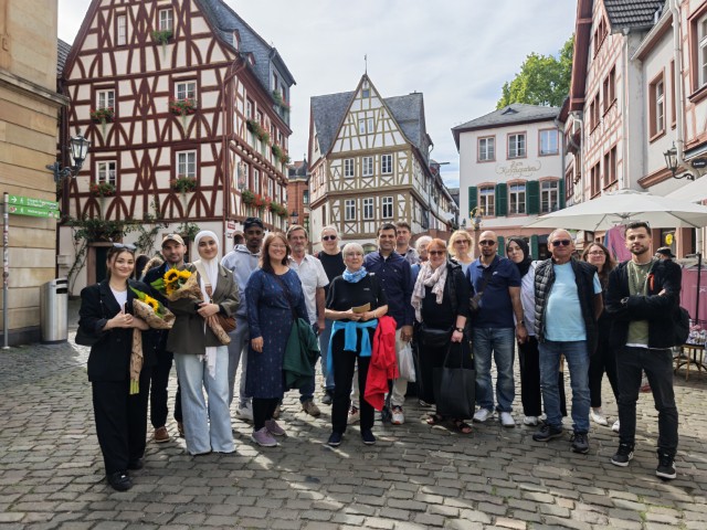 Gruppe bei einer Stadtführung vor historischen Fachwerkhäusern in der Mainzer Altstadt. Die Teilnehmenden stehen gemeinsam auf einem Platz in Mainz